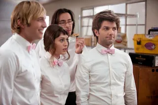 a group of caterers with pink bowties stand in a kitchen in party down