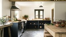 A large kitchen with a wooden island in the middle as well as black painted lower kitchen cabinets with double doors and open shelving on one side