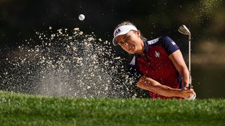 Lexi Thompson of Team USA plays a shot from the bunker in her red and blue uniform and white visor.