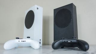 The white Xbox Series S next to the black Xbox Series X standing up vertically on a desk