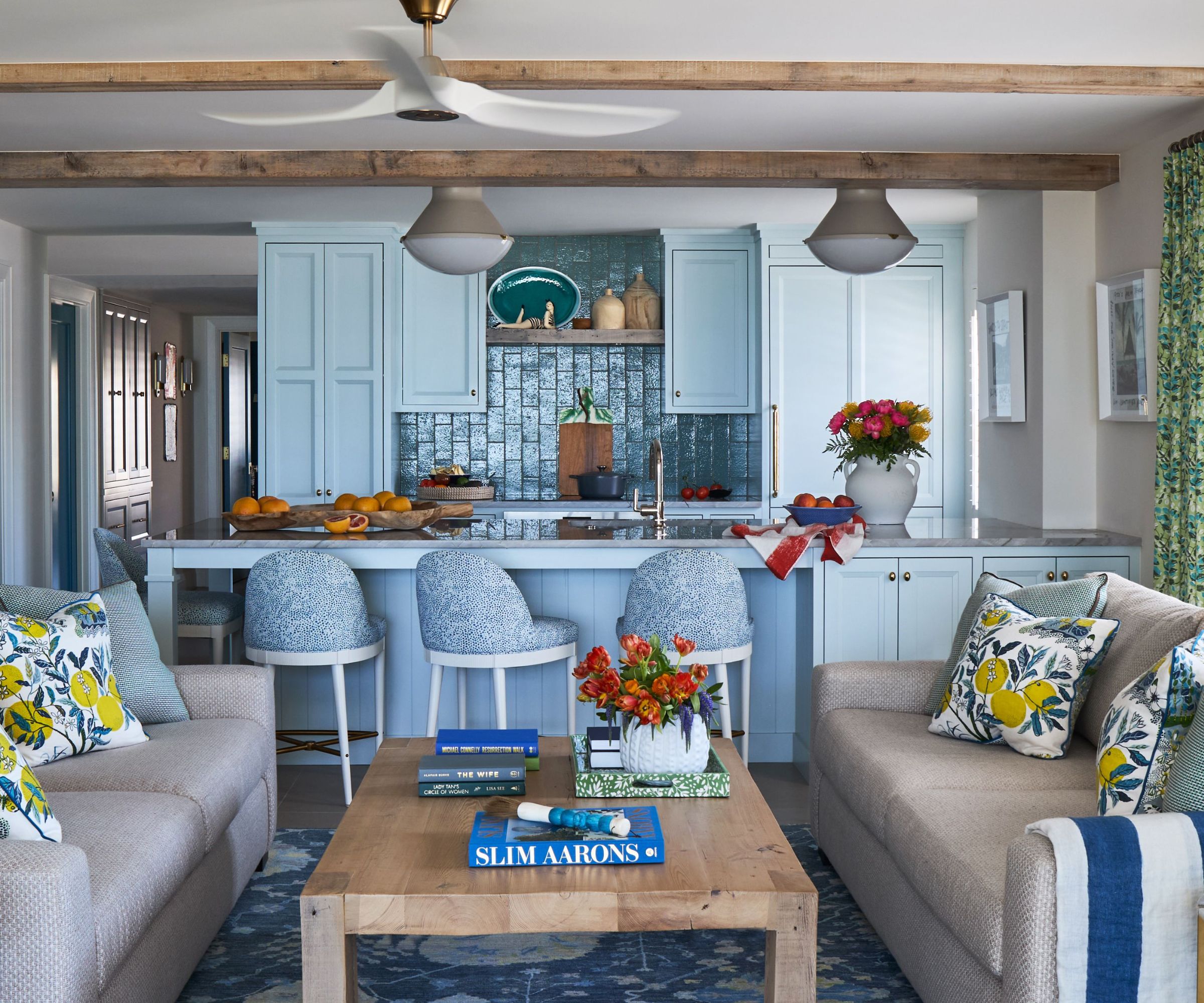 An open plan living space with a view of a blue kitchen. Walls are painted Cloud White OC-130, and the cabinets are painted in Ocean Aire 2123-50, both Benjamin Moore paint colors