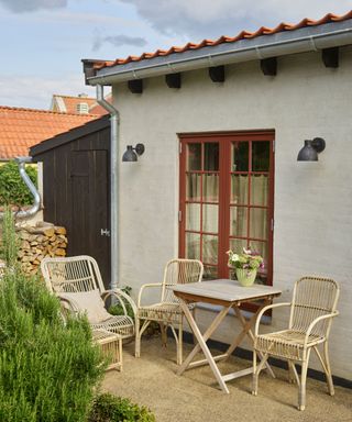 white home exterior with red window frames, outdoor table with chairs