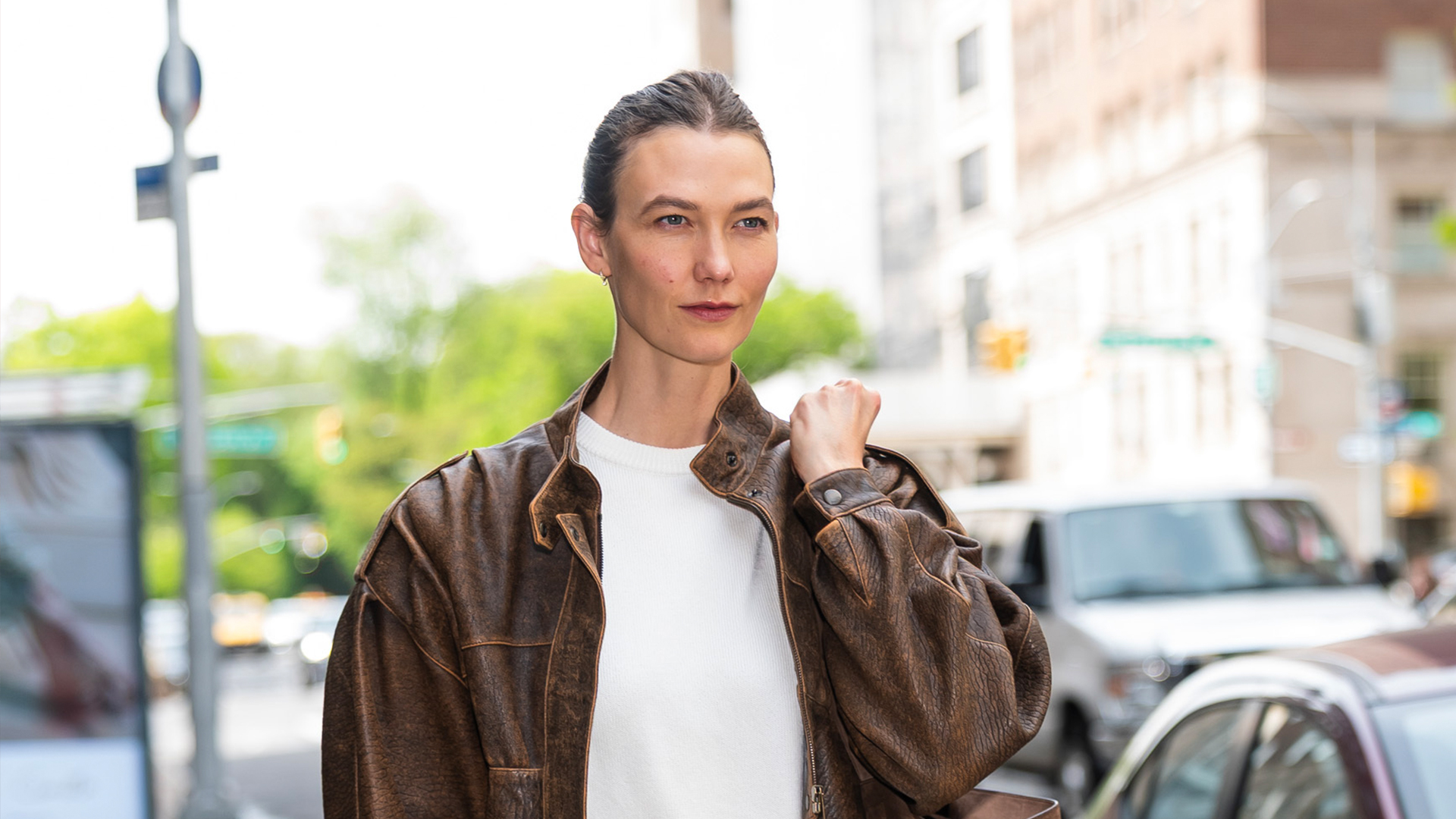 Karlie Kloss wearing a brown leather jacket, white tee, white pants, and black flats 