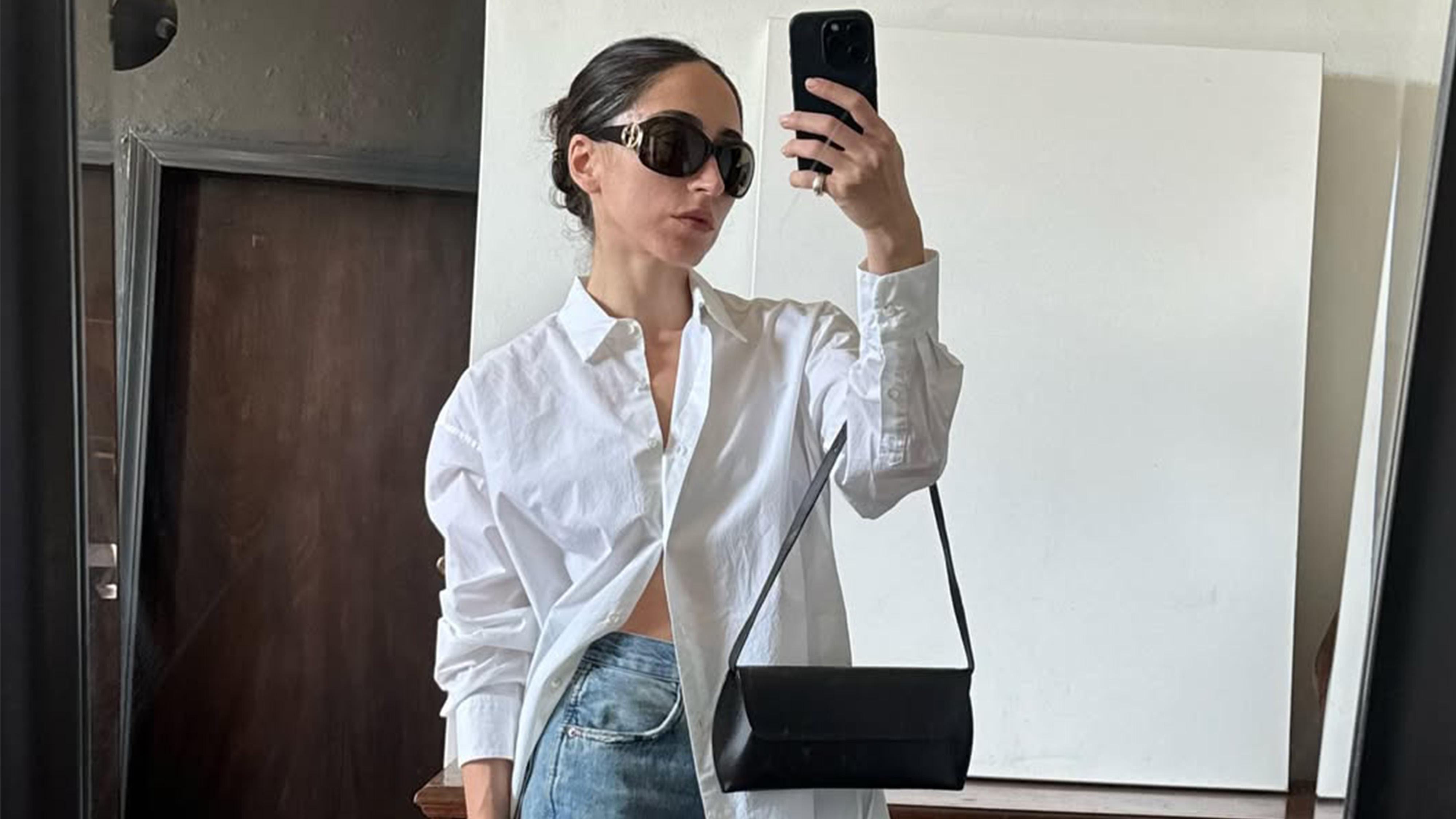 Alexis Badiyi taking a mirror selfie in a white button down with black sunglasses.