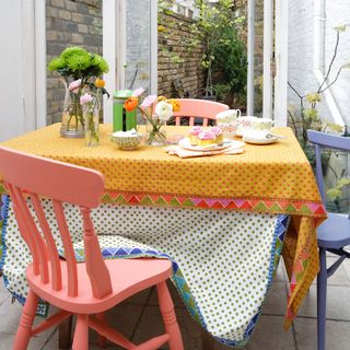 Brightly coloured conservatory with patterned tablecloths and pink and blue chairs