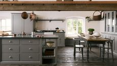 A large traditional kitchen with exposed wood ceiling beans, a large kitchen island, a dining table, and gray cabinetry