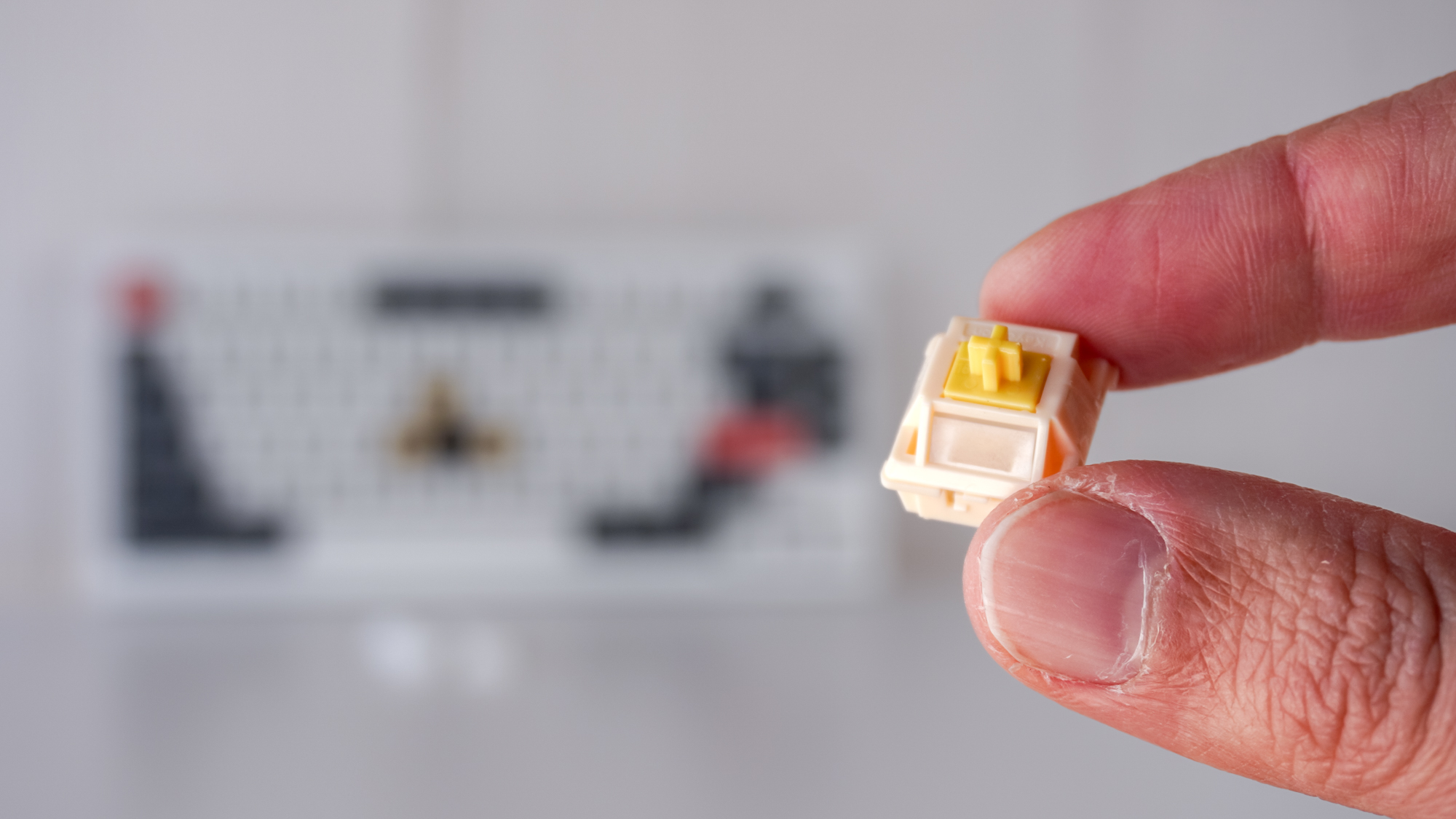 A person holding one of Keychron's Silk POM Switches in front of the Keychron Q1 Ultra 8K on a table