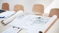 set of architect blueprints on a large table with four chairs in the background