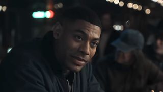 John Stewart smiling in a bar in the Lanterns trailer.