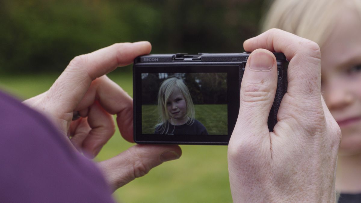 A hand holding the Ricoh GR IIIx camera