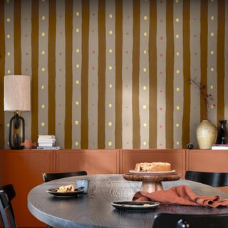 A dining room with hand-painted vertical stripes and dots on the wall with a red terracotta sideboard and a round dining table