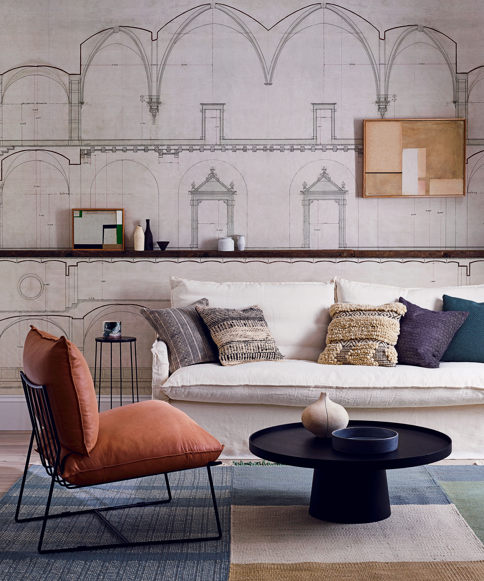 An orange chair next to a white sofa and architectural wallpaper