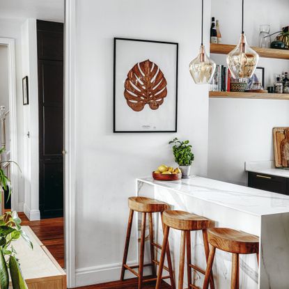 Marble kitchen island with wooden bar stools, wall art, light fixtures