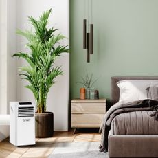 Bedroom with grey bed, green wall and white air conditioning unit.