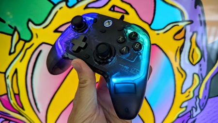 A GameSir Kaleid for Xbox Wired Controller with glowing blue and purple lights is held up against a colorful, abstract background, conveying a vibrant and playful mood.