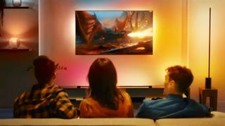 Three people sitting on a couch watching TV with a Philips Hue Sync setup