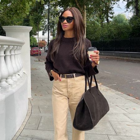 Lorna wears a brown sweater, beige jeans and carries brown suede bag