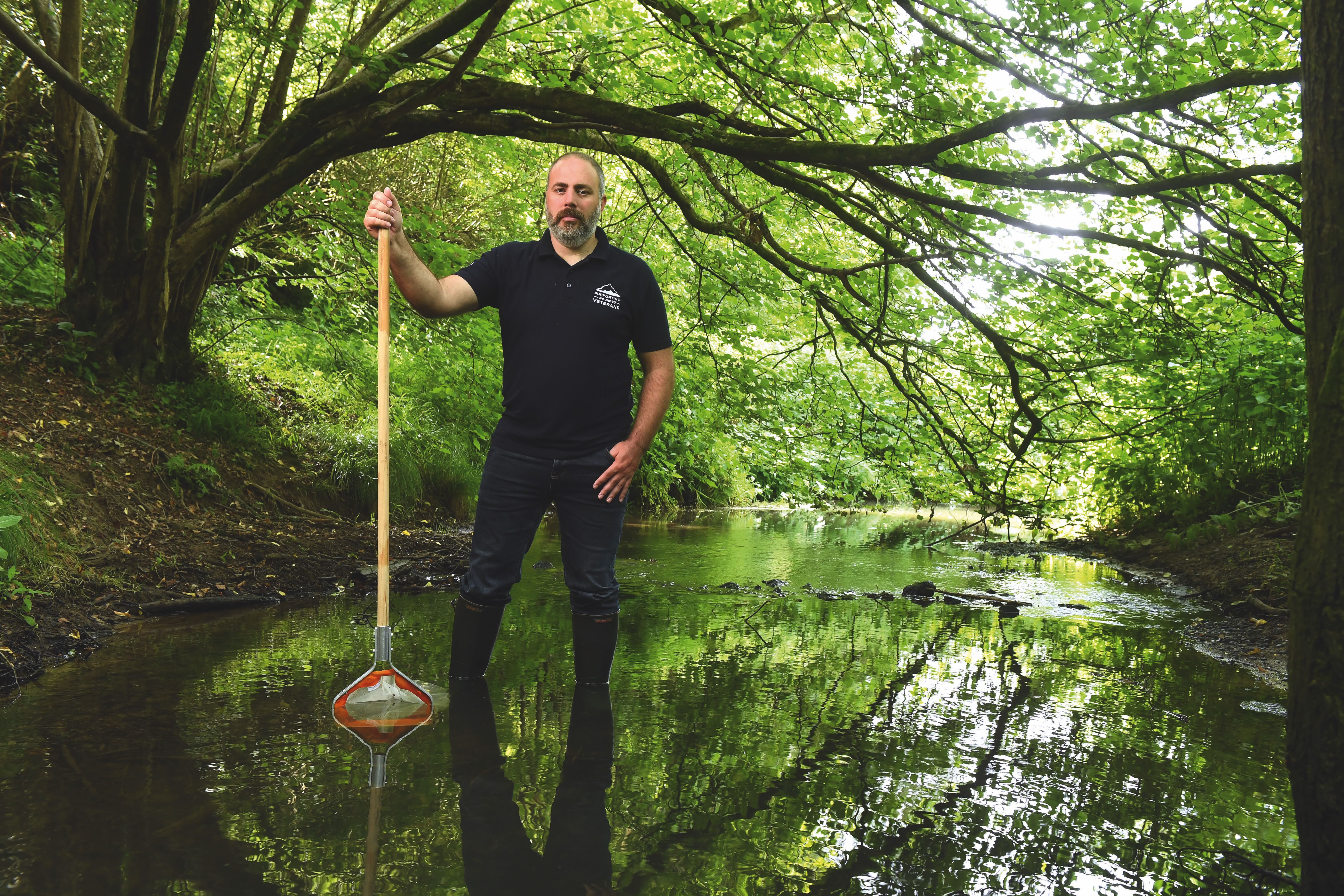 Phil Wright stands in a woodland pool holding a net like a staff looking into the camera