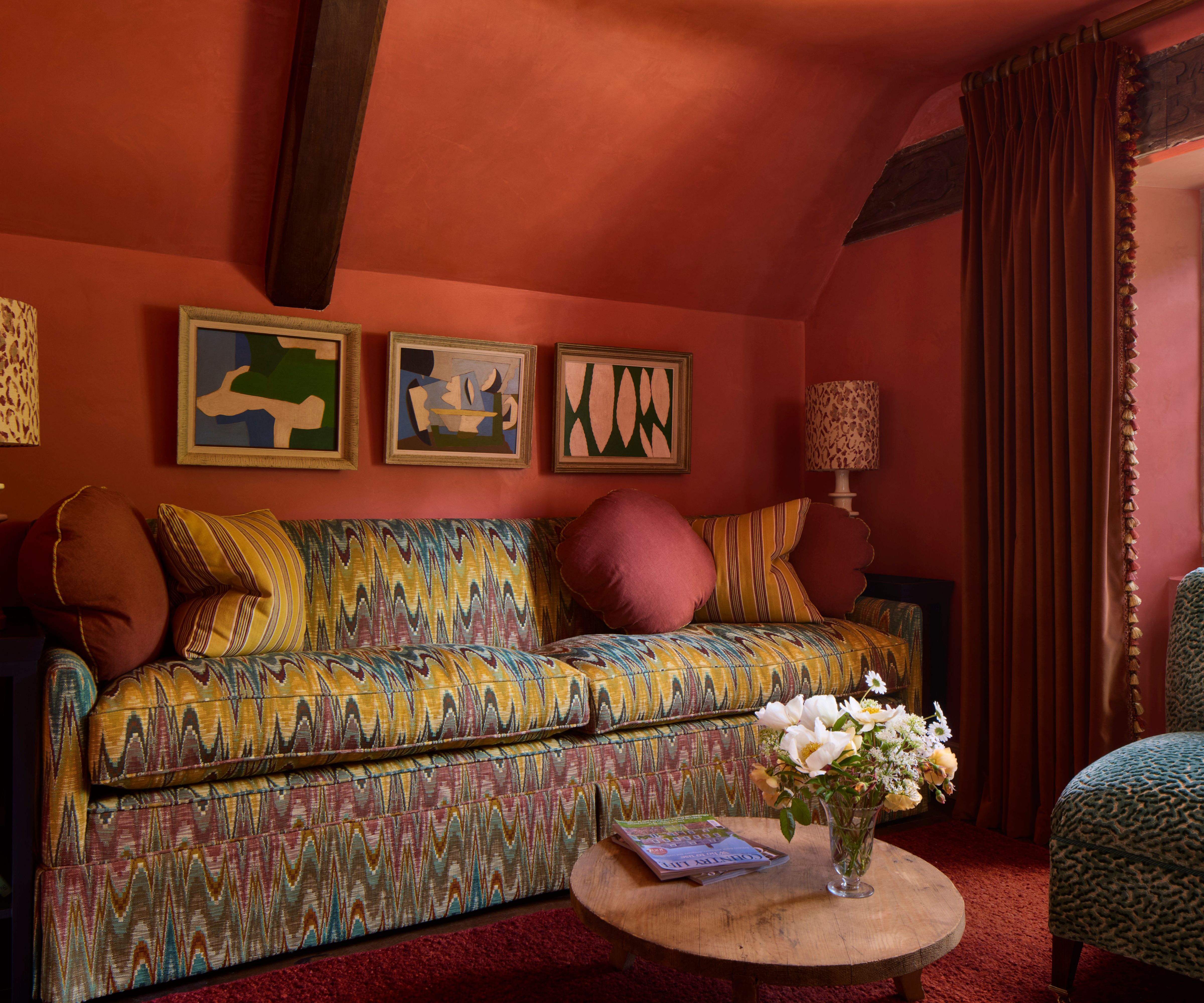 a dark red orange living room color drenched in rich color styled with a Missoni-style printed couch with yellow striped pillows and red round cushions