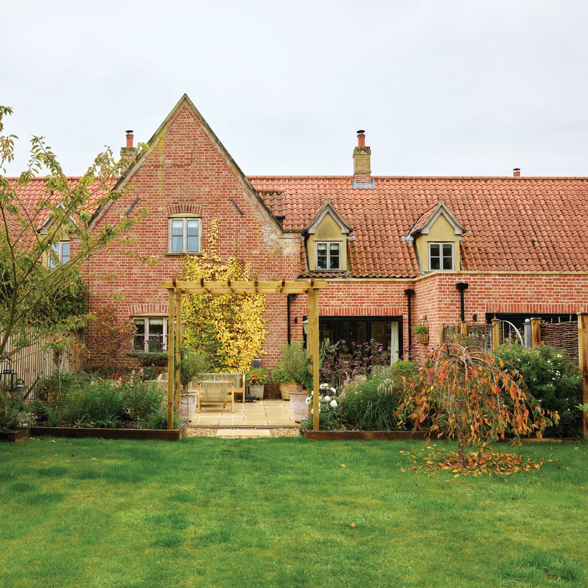 Exterior of house from the back with grassed garden, pergola, shrubbery and bricked exterior