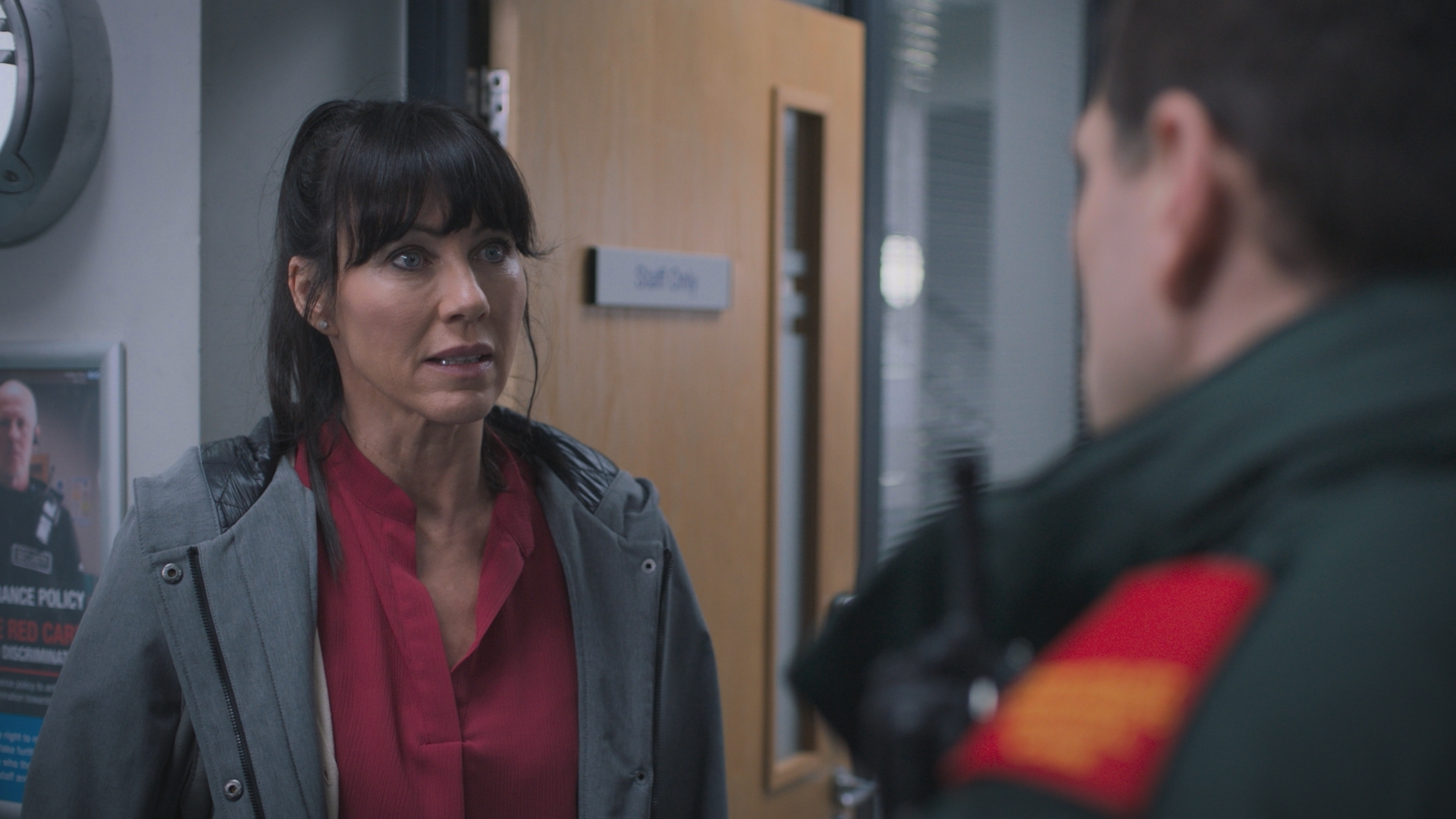 Faith looks at Iain with trepidation as they stand in a hospital corridor.