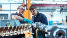 Senior engineer showing machinery to apprentice in a warehouse setting.