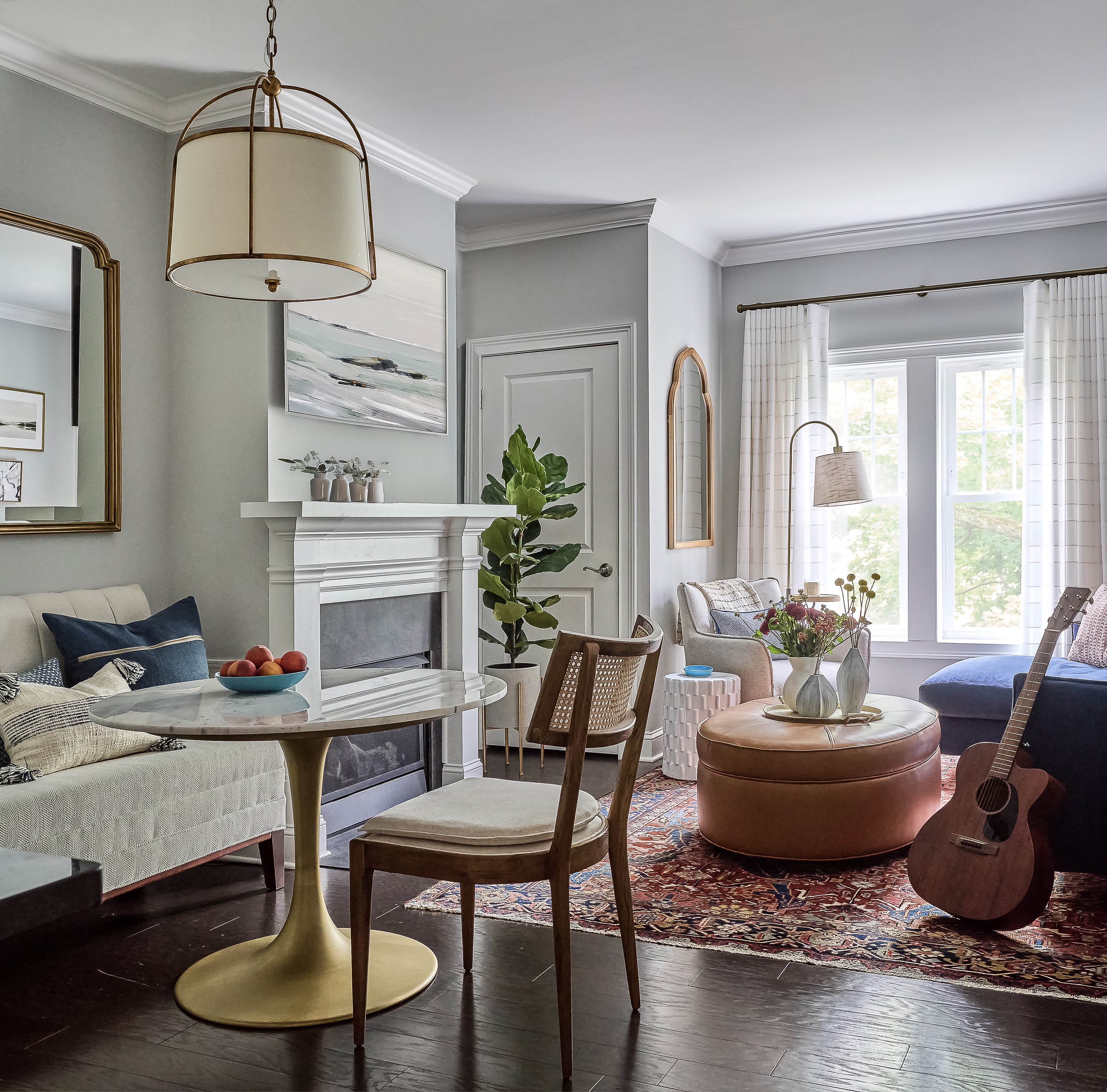open plan living/dining apartment space with dark hardwood floor, vintage rug, round dining table, blue couch, round leather footstool, mirrors, floor lamp, pendant lamp