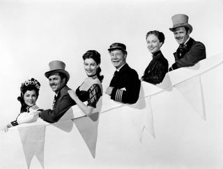 a captain and a group of people on a fancy cruise ship look over the edge in show boat