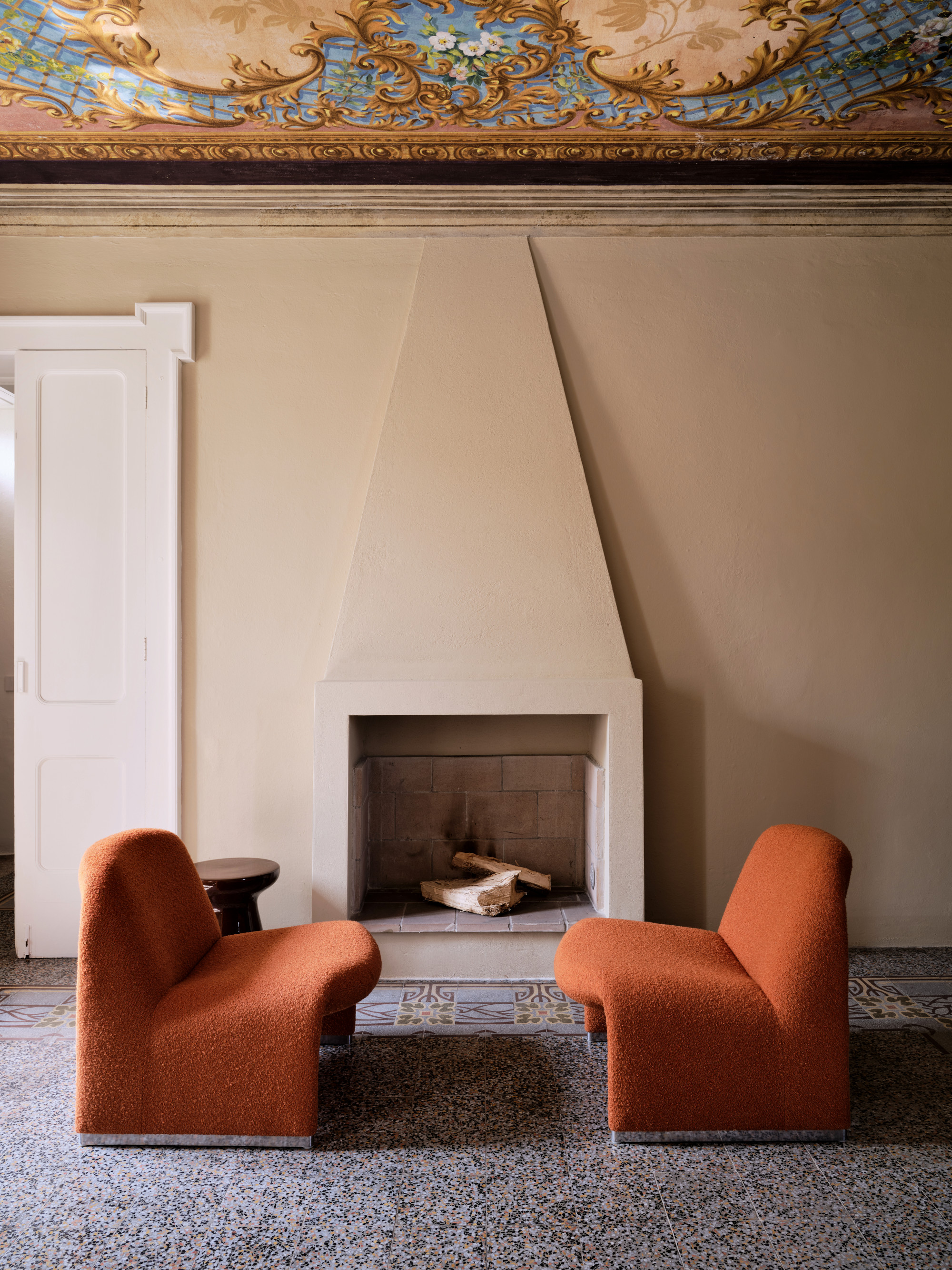 Seating area in front of a minimalist fireplace with painted ceiling, rust accent chairs and terrazzo floor