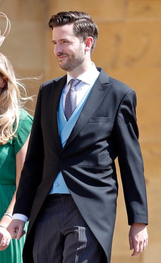 Jason Knauf wearing a dark suit and blue vest walking outside on a sunny day