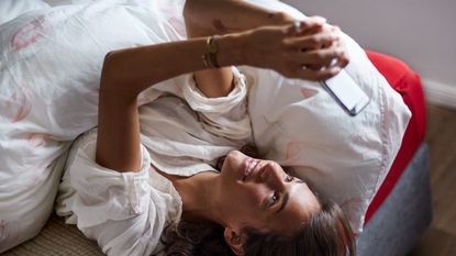 Relaxed young woman using cell phone in bed - stock photo