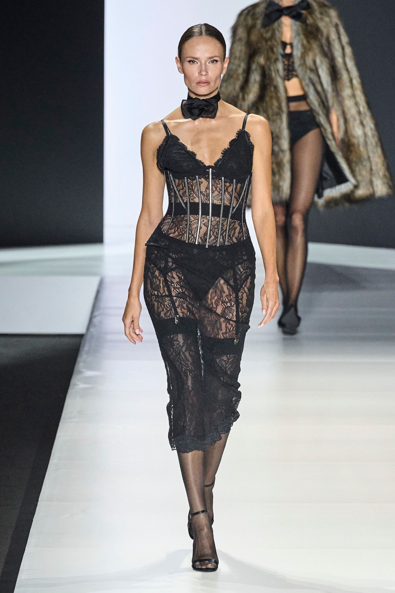 A model walking in the S/S 25 Dolce & Gabbana show wearing a black lace sheer dress.