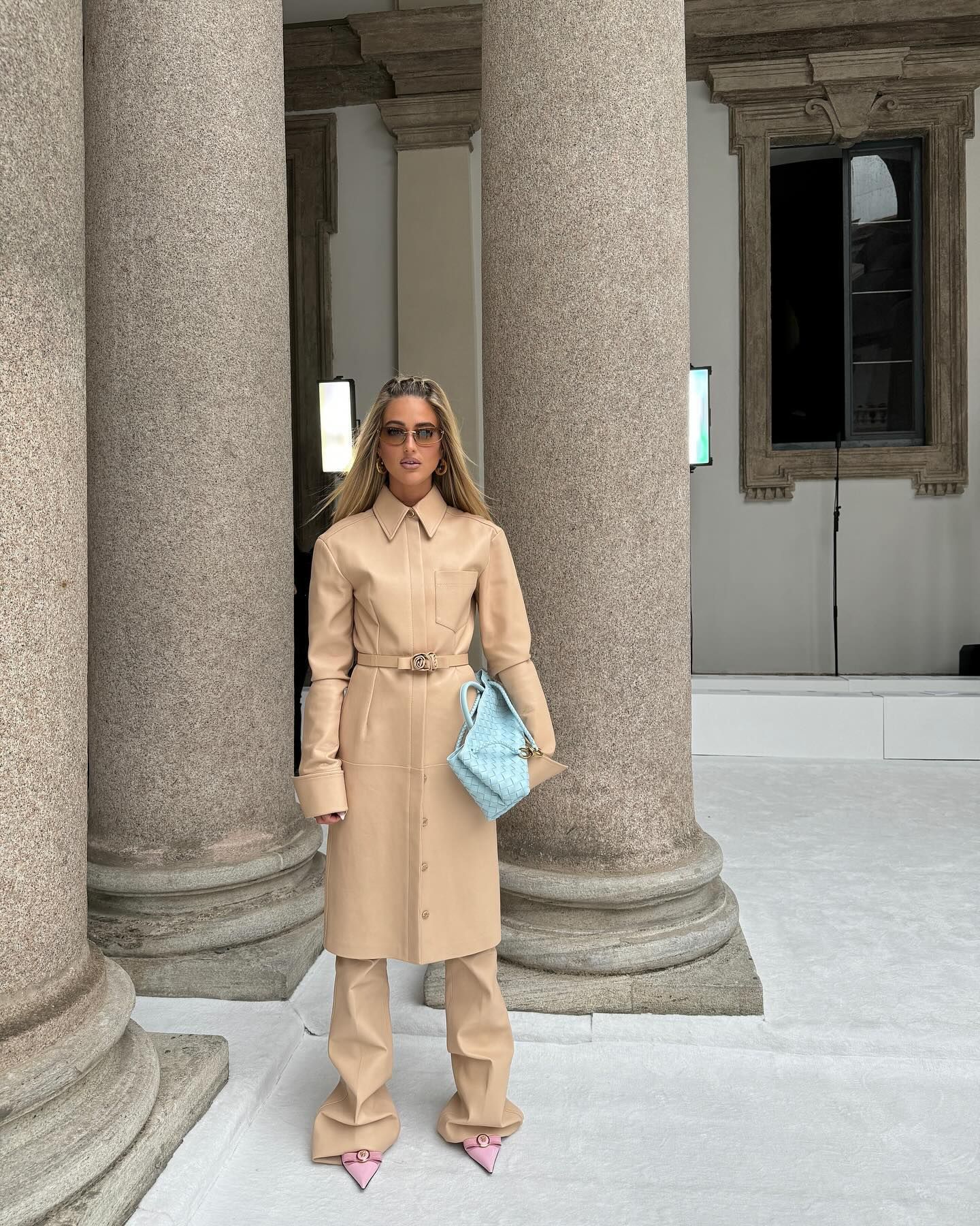Woman wearing nude tan leather coat, matching leather pants, and baby blue Bottega Veneta bag
