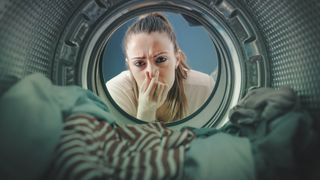 A woman holding her nose while looking into a smelly washing machine