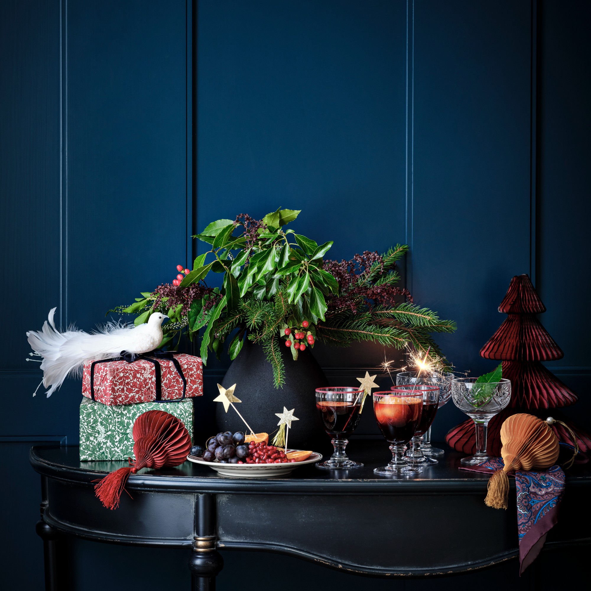 An antique black console table against a dark blue wall displaying Christmas decor