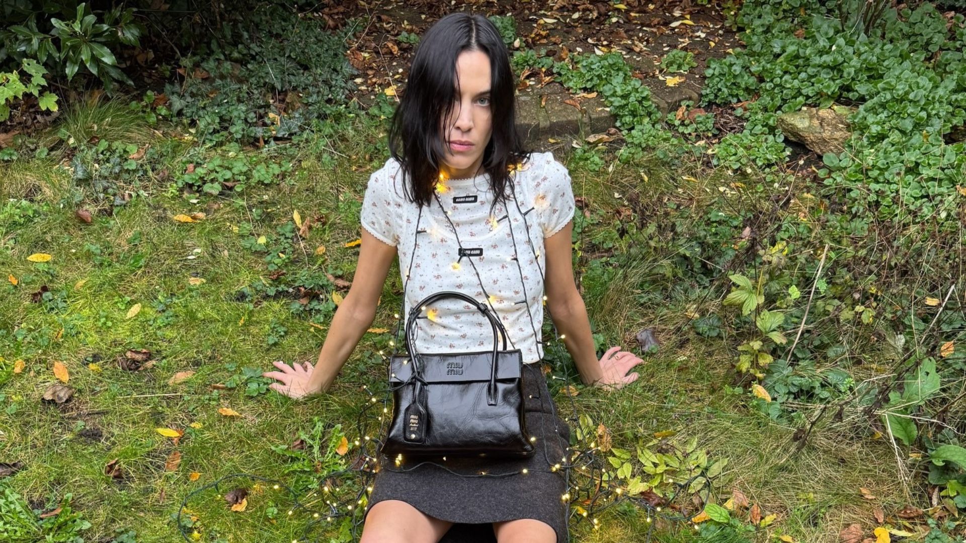 Alexa Chung sits in a garden wearing a layered top, a wool miniskirt and Miu Miu&#039;s Mary Jane loafers.