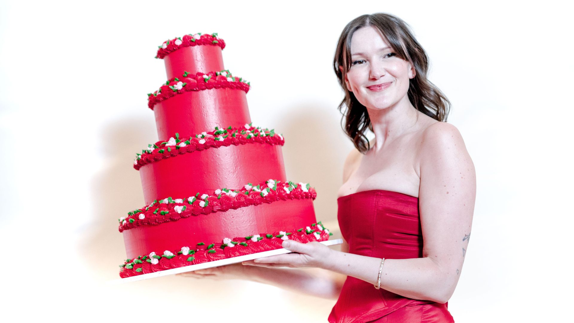 Lily Vanilli holds a red cake and wears a red dress