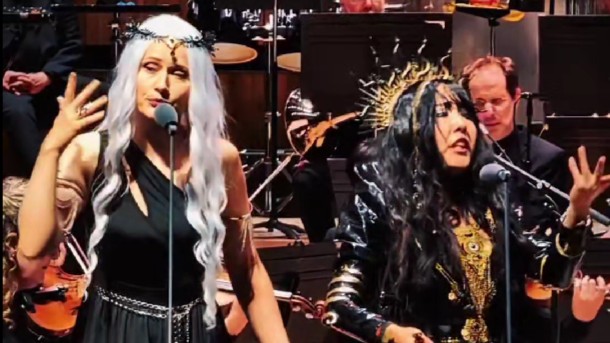 Two women, each with a microphone, singing. They are both dressed in Diablo-themed outfits.