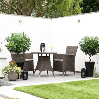 Corner of a garden with white rendered walls and a black wicker-style dining set