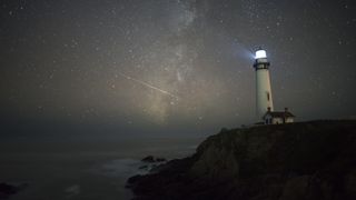 A shooting star streaks behind a lighthouse on a starry night