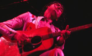 Jimmy Page plays an acoustic guitar onstage with Led Zeppelin in 1977