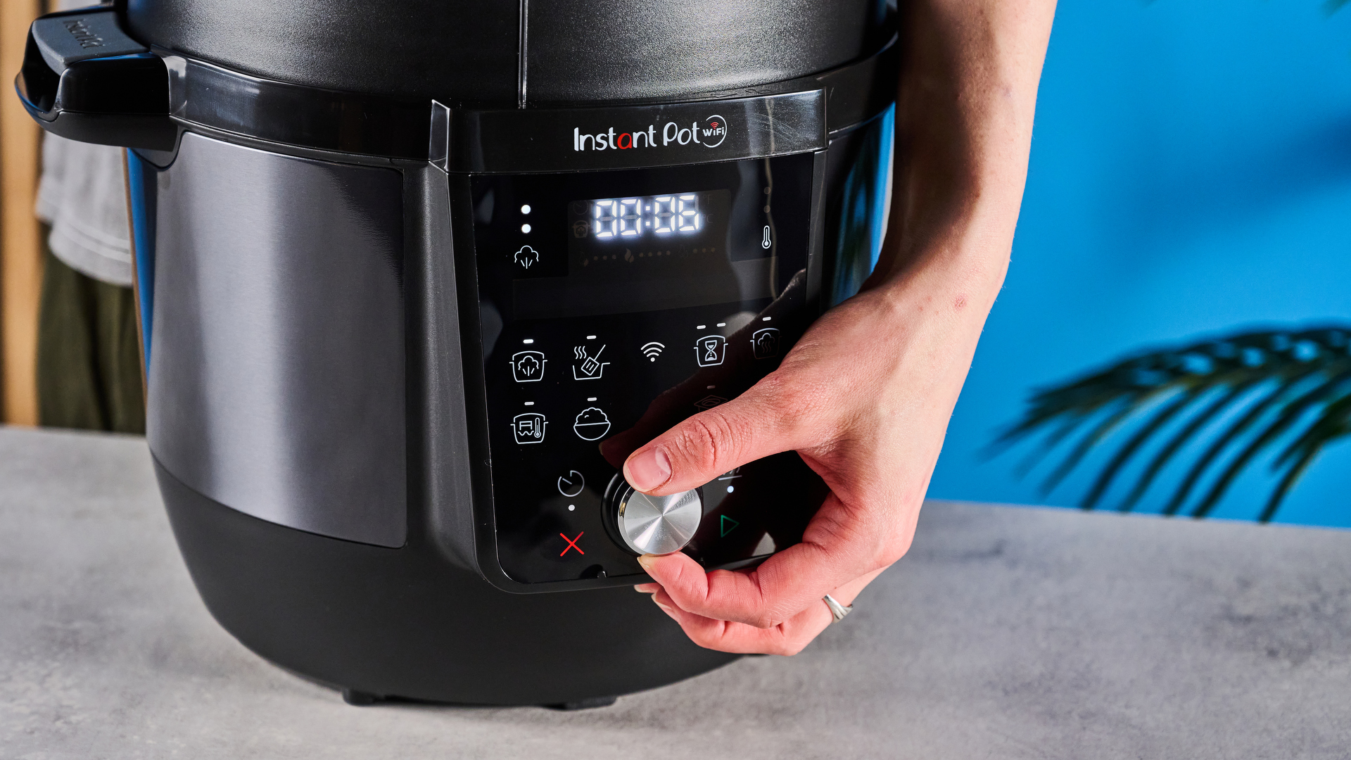 Instant Pot Plus photographed in front of a blue background.