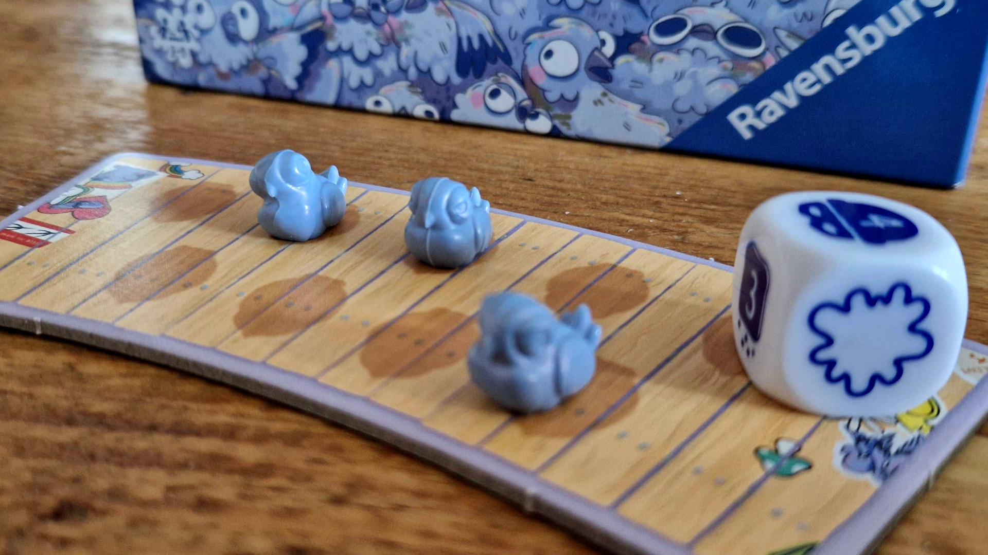 Oh My Pigeons tokens on a board, with a die beside them