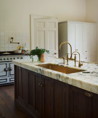 A white kitchen with marble countertops and a statement dark wood kitchen island