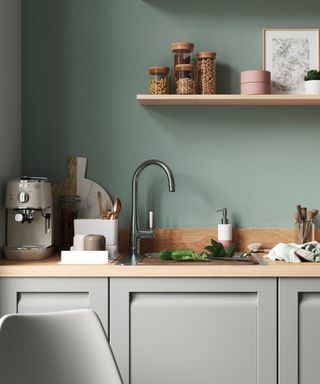 A compact kitchen with a modern, minimalist design featuring soft green walls and light gray shaker-style cabinets.