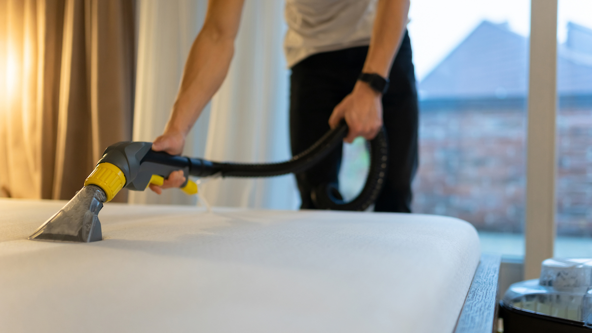 A man cleans the top of a mattress with a vacuum cleaner