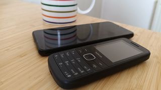 Two phones next to each other on desk, in front of a cup