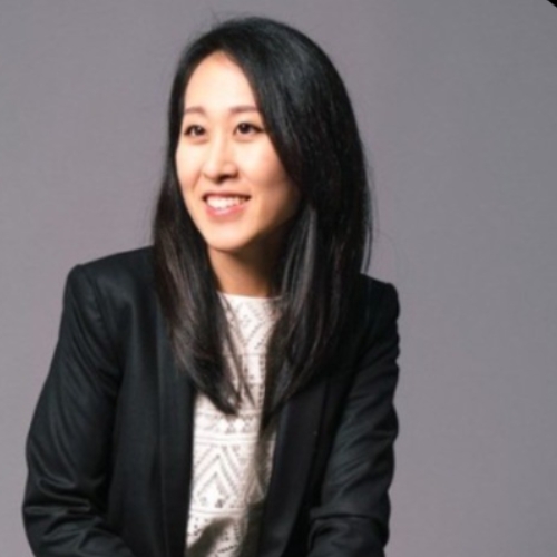 Profile image of a woman in a white top and black blazer sitting in front of a purple background.