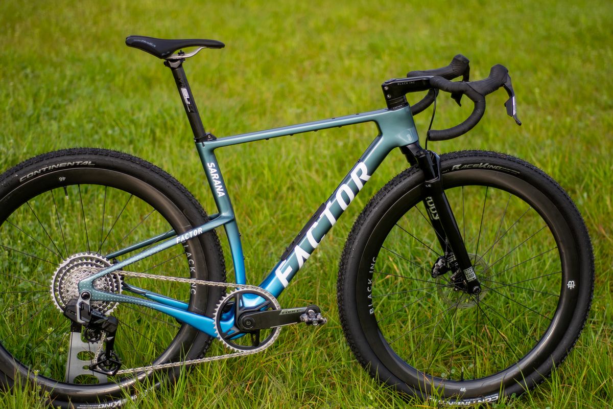 A blue Factor Sarana gravel bike in a grassy field with a hedge in the background