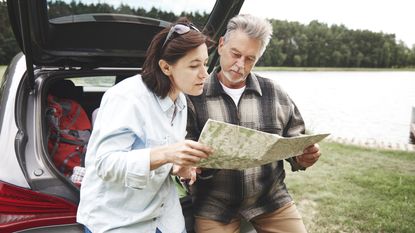 An older couple look at a map together outside their SUV.